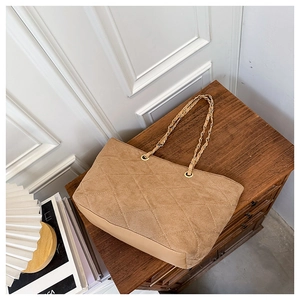 Detail of brown corduroy quilted tote bag with gold chain strap on wooden surface