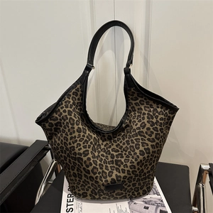 Leopard print canvas tote bag with black faux leather handles on a minimalist chair