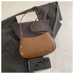 Detail of brown crocodile pattern shoulder bag with heart patch and silver rivets