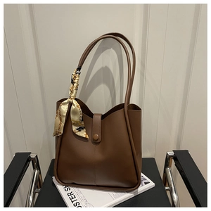 Detail of dark brown leather tote bag with silk scarf on handle over a magazine
