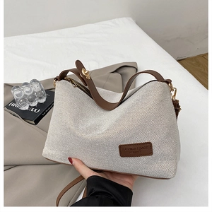 Detail of cream canvas bag with brown leather strap and brand label in minimalist setting