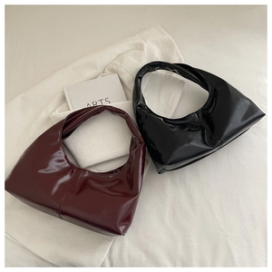 Flat lay view of minimalist black and burgundy leather crescent underarm bags on white fabric