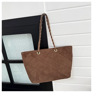 Detail of dark brown quilted tote bag with matte texture and golden chain strap