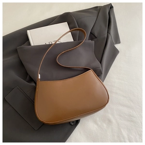 Flat lay of a vintage brown leather underarm bag on a suit jacket and art book