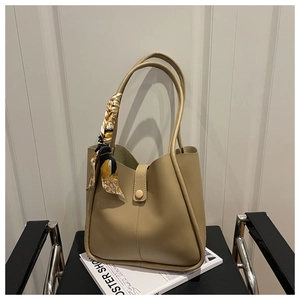 Close-up of beige tote bag with a patterned silk scarf handle on a black leather bench