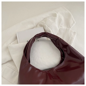 Close-up of deep burgundy crescent handbag with glossy finish on velvet background