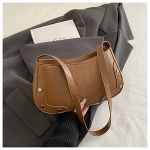 Detail of brown crocodile pattern crescent bag with heart patch and metal rivets