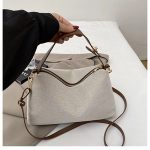 Detail of cream woven texture handbag with brown leather straps and gold metal zippers