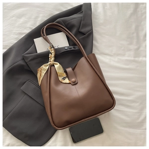 Detail of dark brown tote bag with decorative scarf and buckle on a grey blazer