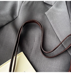 Gros plan sur la bandoulière en cuir marron sur costume gris pour un style minimaliste