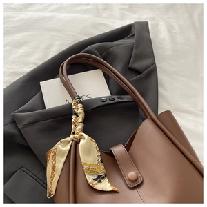 Close-up of brown tote bag with silk scarf detail on gray suit and decorative book