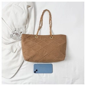 Flat lay of brown quilted suede tote bag with metal chain handles and a mobile phone