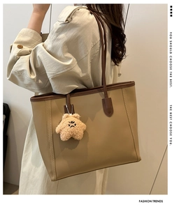 Detail view of large beige tote bag with brown trim and plush star charm on the shoulder