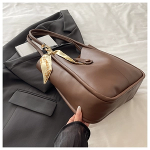 Detail of coffee brown leather tote bag with elegant silk scarf on the handle