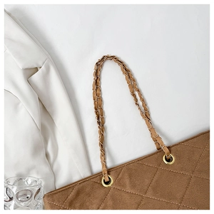 Detail of brown quilted tote bag showing matte texture, golden eyelets and chain strap