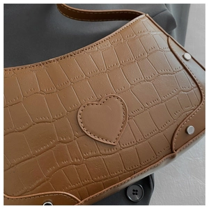 Detail of brown crocodile pattern shoulder bag with heart patch and metal rivets