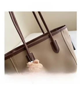 Detail view of contrast color stitching and plush bear charm on a faux leather tote bag