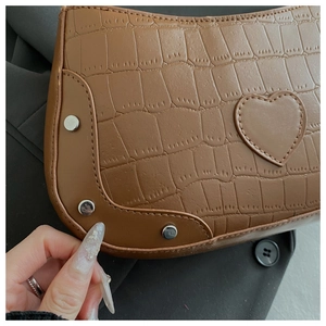 Detail of brown crocodile pattern shoulder bag with heart patch and silver rivets