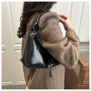 Close-up of black glossy shoulder bag with leather texture on a wool coat