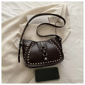 Détail du sac demi-lune marron foncé avec rivets argentés et boucle sur un blazer