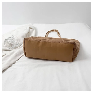 Detail of brown quilted tote bag with diamond pattern and metal chain shoulder strap