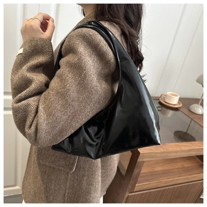 Side view of a black patent leather crescent shoulder bag worn with a brown blazer