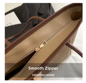 Detail of smooth gold zipper closure and brown trim on beige PU leather tote bag