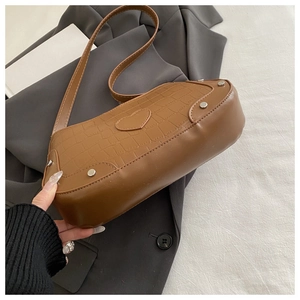 Detail of brown faux crocodile leather crescent bag with heart patch and metal rivets