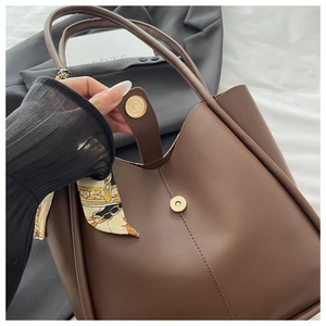 Detail of brown tote bag with magnetic closure and decorative silk scarf handle wrap