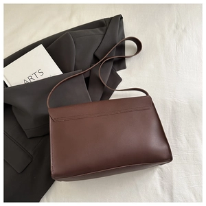 Detail of a brown matte leather shoulder bag laid on a gray blazer and white fabric
