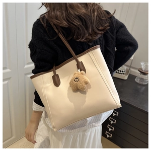 Detail view of large cream tote bag with brown straps and cute plush pendant charm