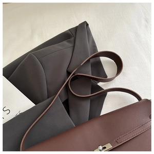 Detail of a dark brown leather tote bag with metallic turn-lock over a grey blazer
