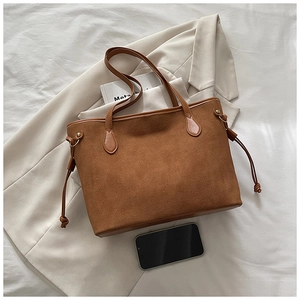 Dettaglio di una borsa tote in pelle scamosciata marrone con coulisse e finiture metalliche oro