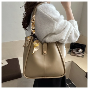 Detail of beige tote bag with smooth texture and decorative scarf on handle for daily use