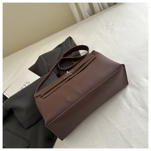 Detail of dark brown leather tote bag with metallic twist lock on office suit background