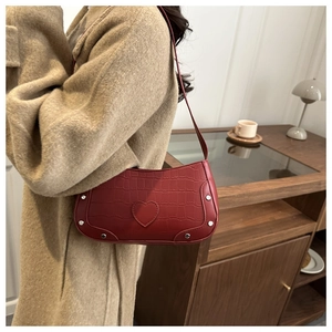 Detail of reddish-brown crescent bag with crocodile pattern and silver rivets on model
