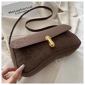 Detail of dark brown matte suede shoulder bag with elegant gold metal buckle on white fabric
