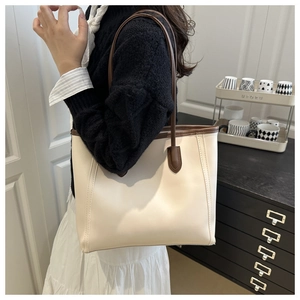 Detail of a large cream tote bag with brown straps worn on the shoulder by a model