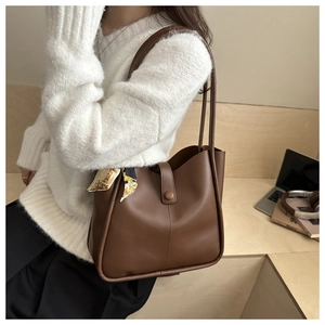 Detail of a brown leather tote bag featuring a decorative printed silk scarf on the strap