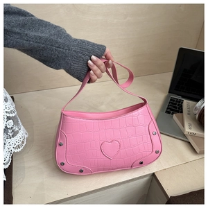 Close-up of pink croc-embossed shoulder bag with heart patch and silver rivet details