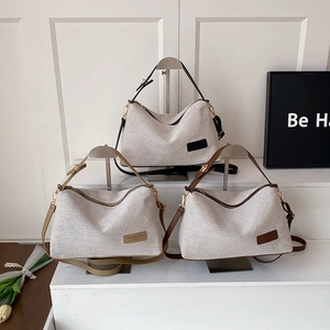 Three canvas shoulder bags with leather straps in black, khaki, and brown on display