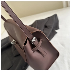 Detail view of smooth brown matte leather texture and silver buckle on tote bag