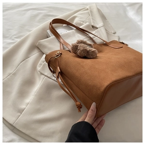 Dettaglio di una borsa tote in pelle scamosciata marrone con orsetto e finiture in pelle