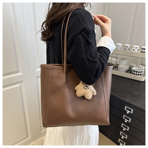 Detail of dark brown leather tote bag with elegant stitching and plush charm