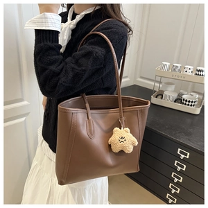Detail view of large brown tote bag with a yellow star plush charm and slender shoulder straps