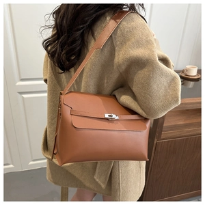 Detail of a brown leather tote bag with silver metal lock on a model in a beige coat