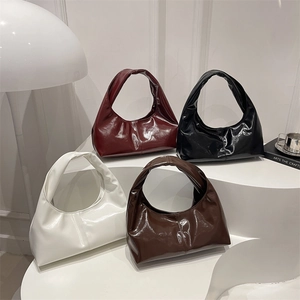 Minimalist patent leather underarm bags in four colors displayed on white steps