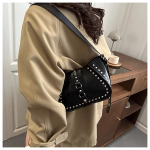 Détail d'un sac besace en cuir noir avec des rivets argentés et une large bandoulière