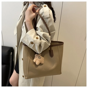 Detail of a beige leather tote bag with brown trim and a plush bear pendant on model