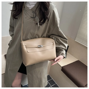 Close-up of minimalist beige shoulder bag with metal turn-lock on trench coat outfit